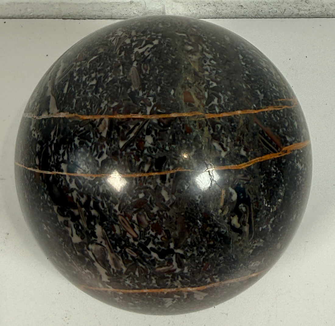 Large Orthoceras fossil sphere from Morocco with visible prehistoric shell fossils in polished black stone. Natural history décor collectible display piece.