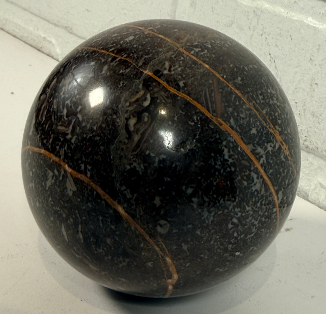 Large Orthoceras fossil sphere from Morocco with visible prehistoric shell fossils in polished black stone. Natural history décor collectible display piece.