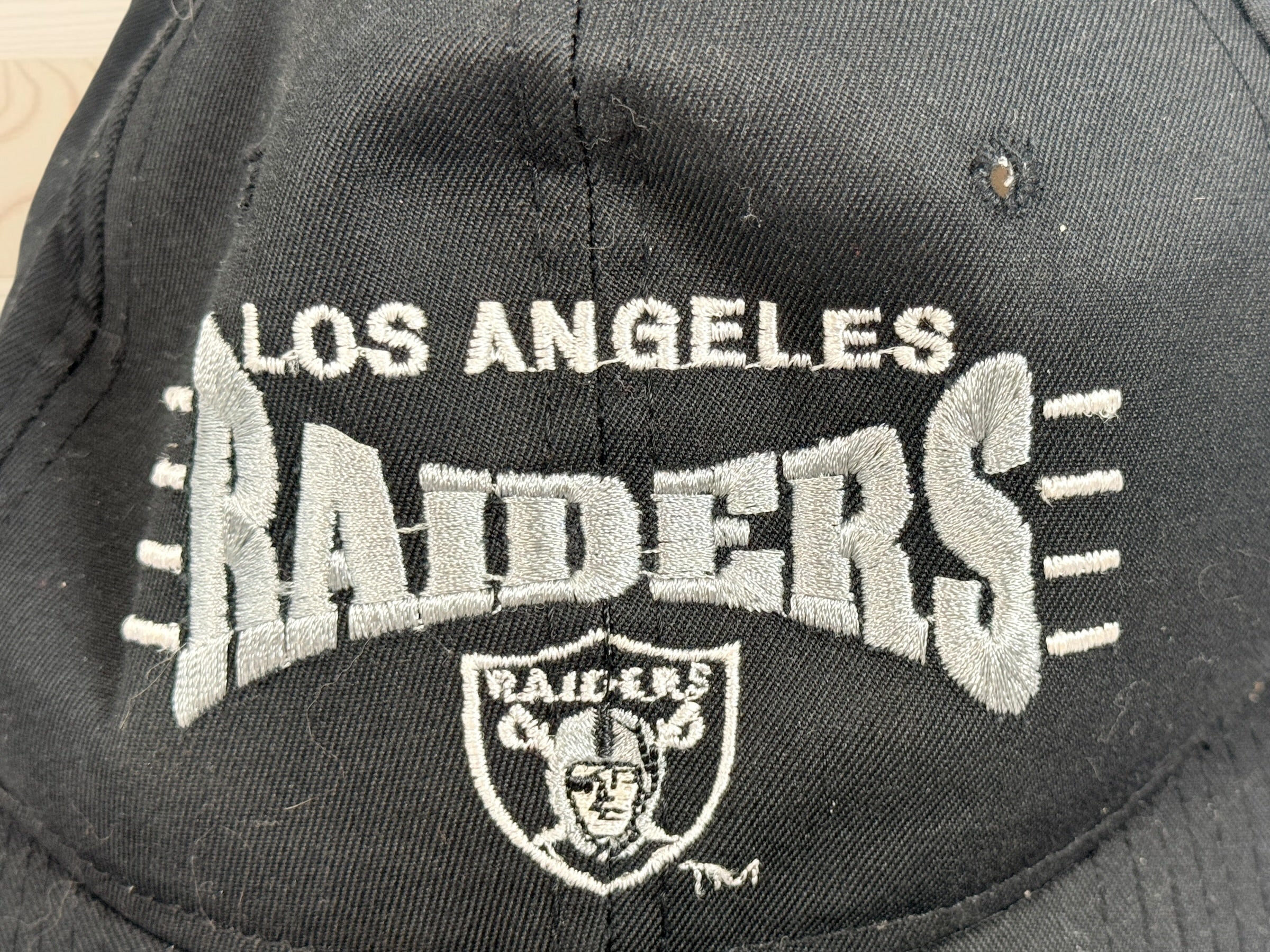 Vintage Los Angeles Raiders snapback hat with green undervisor and embroidered NFL football graphics from the early 1990s.