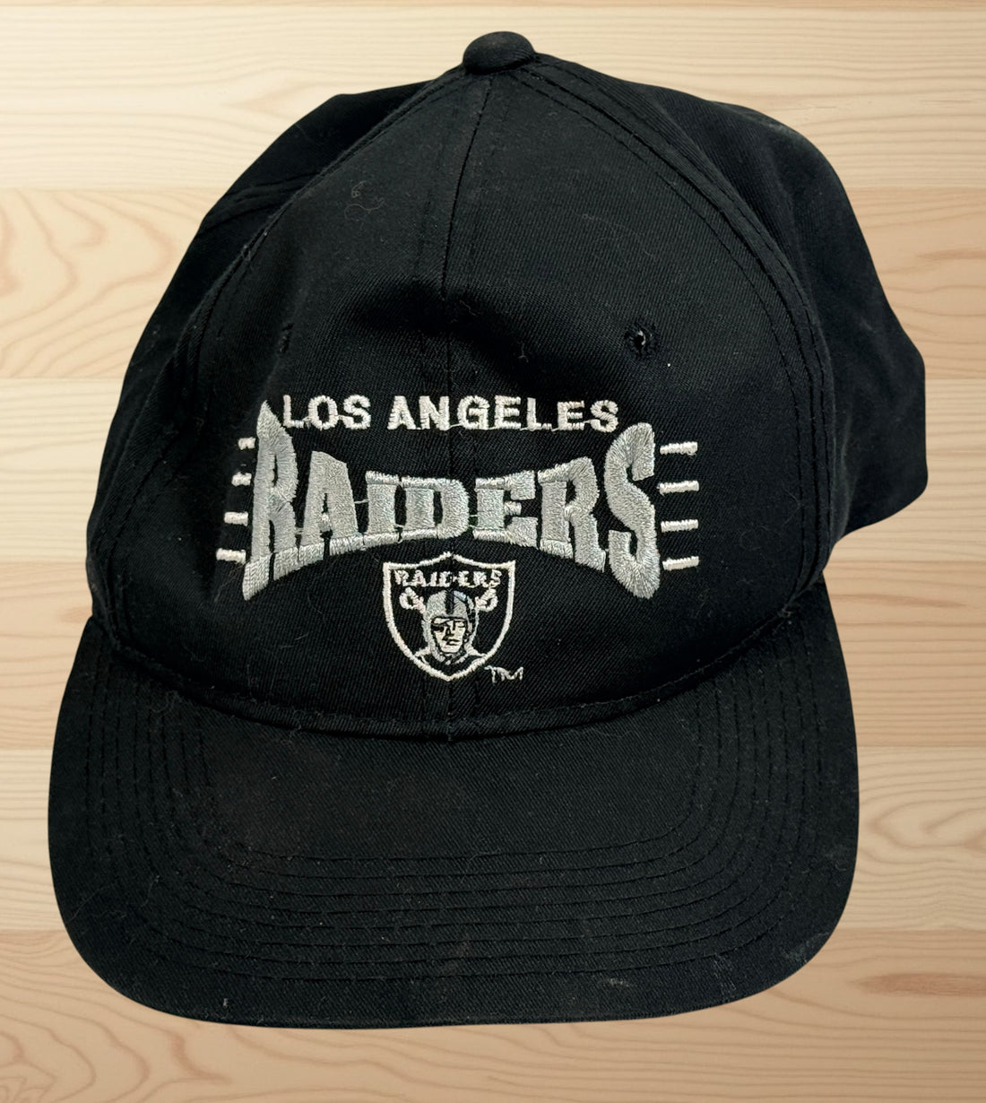 Vintage Los Angeles Raiders snapback hat with green undervisor and embroidered NFL football graphics from the early 1990s.
