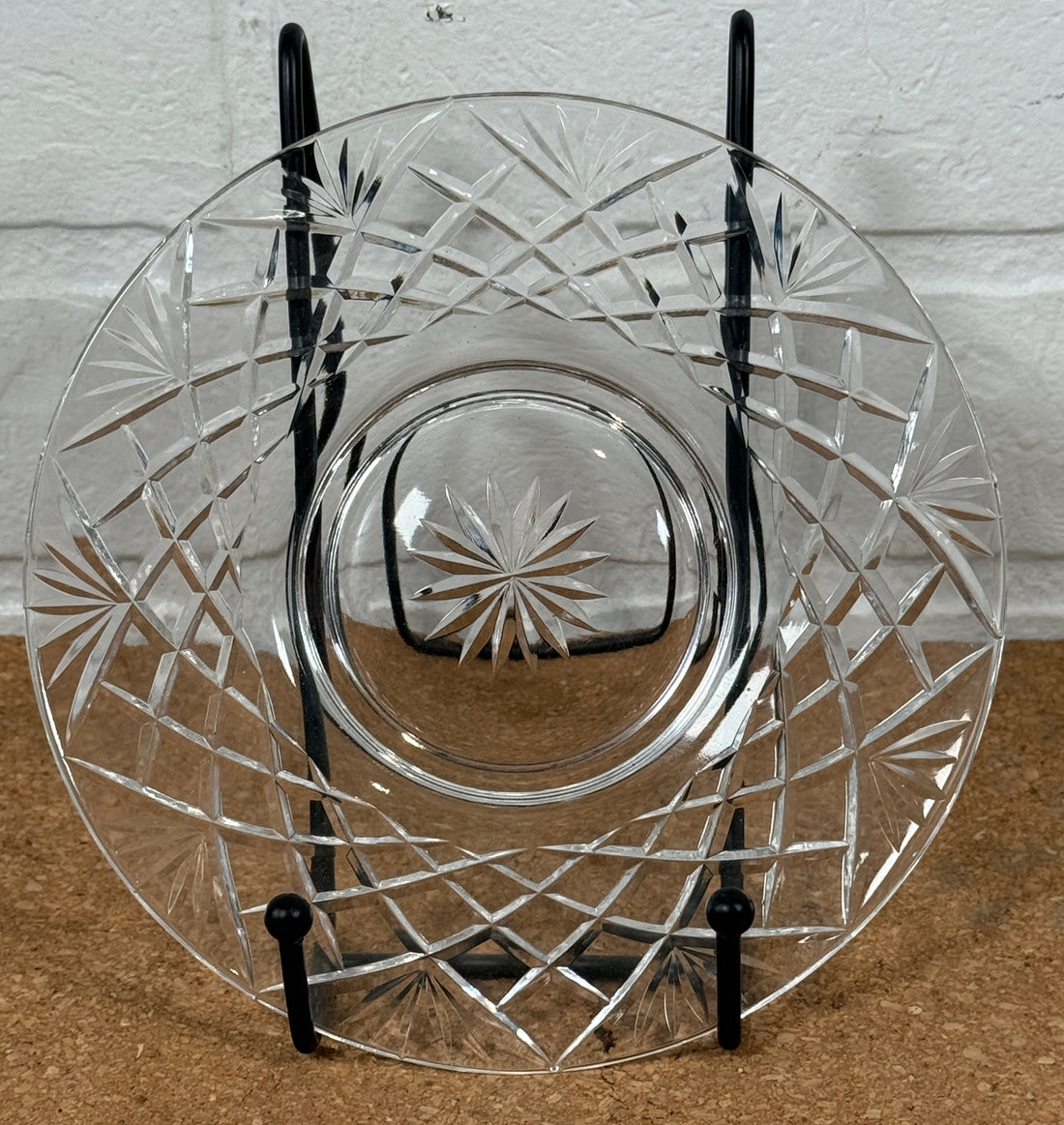 Cut crystal glass plate on a stand with a white brick wall background