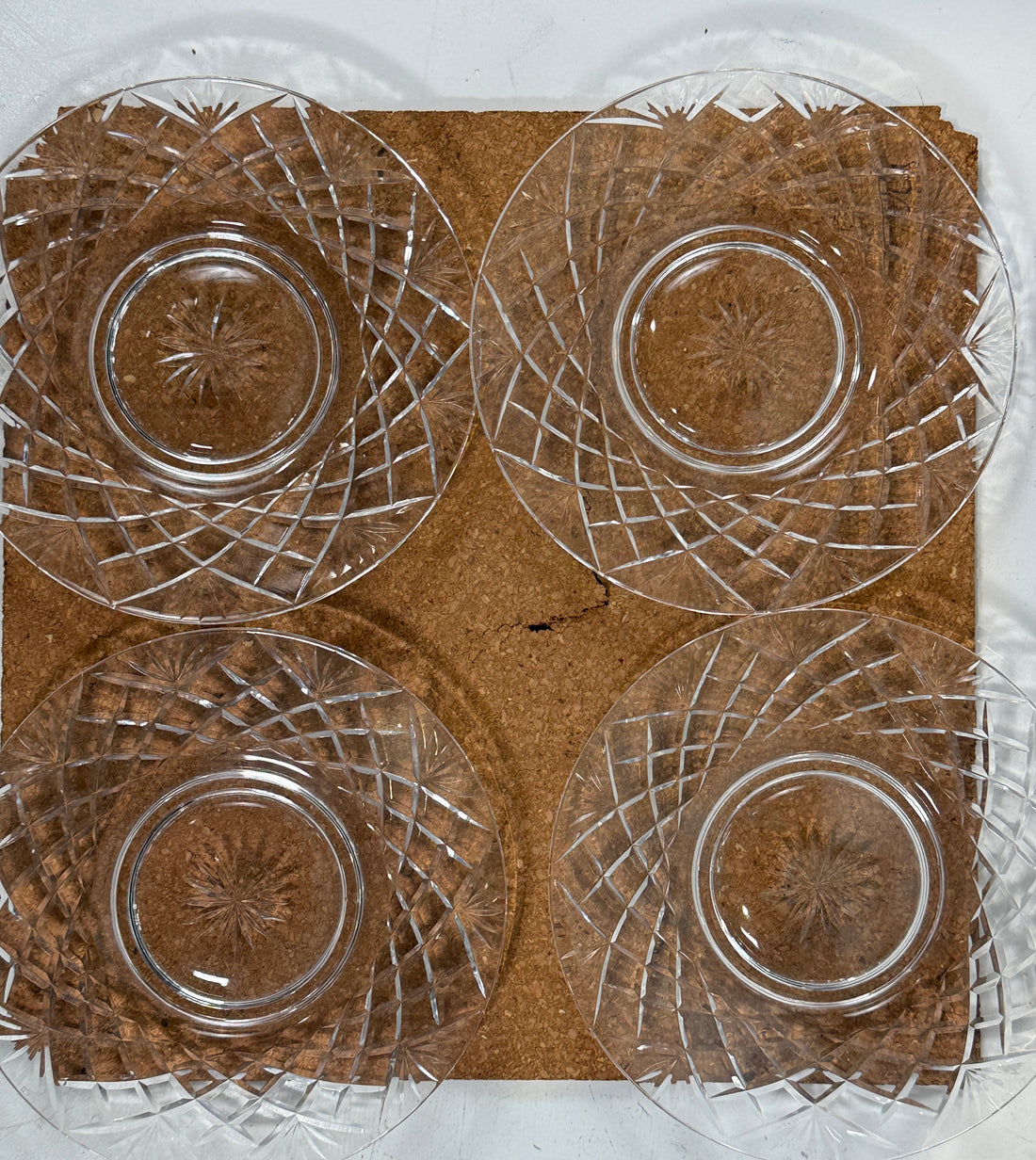Four clear glass plates with intricate designs on a brown cardboard background