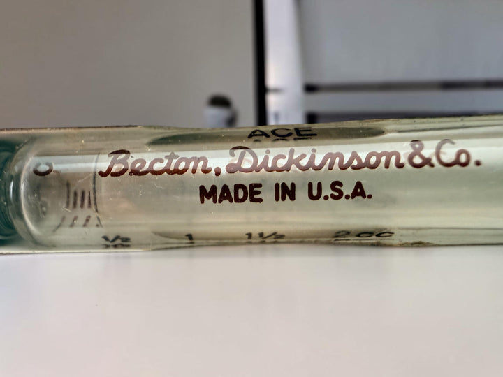 Vintage BD Yale Luer-Lok glass hypodermic syringe with original box. Mid-century medical collectible made in USA for apothecary or scientific display.