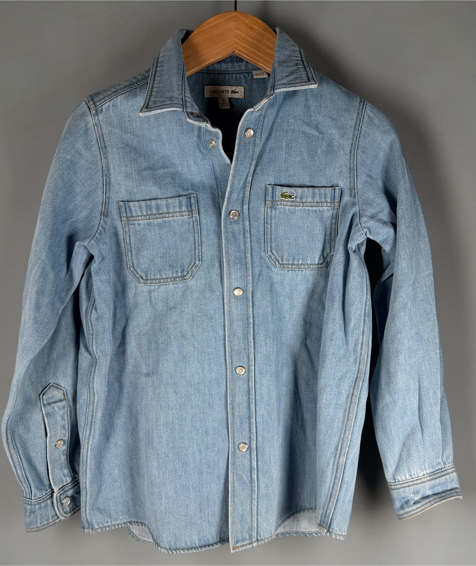 Authentic Lacoste kids denim overshirt in size 8 featuring snap-button closure, chest pockets, and classic crocodile logo. Light wash designer children’s wear.
