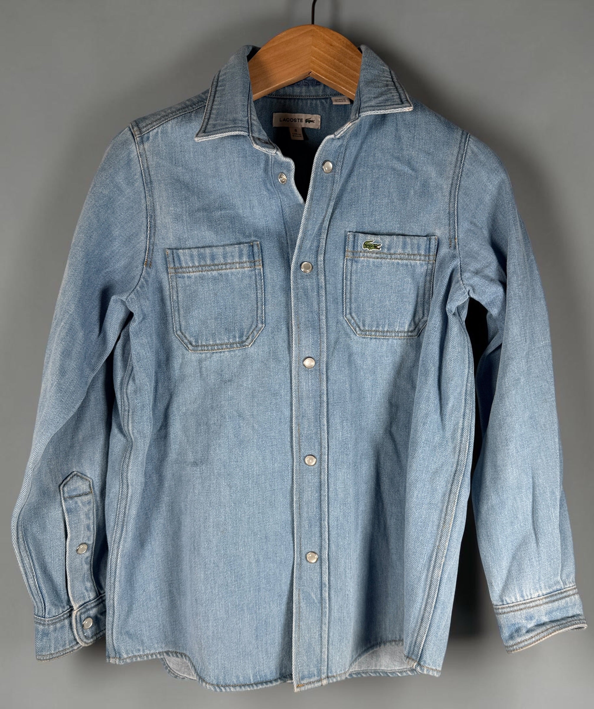 Authentic Lacoste kids denim overshirt in size 8 featuring snap-button closure, chest pockets, and classic crocodile logo. Light wash designer children’s wear.