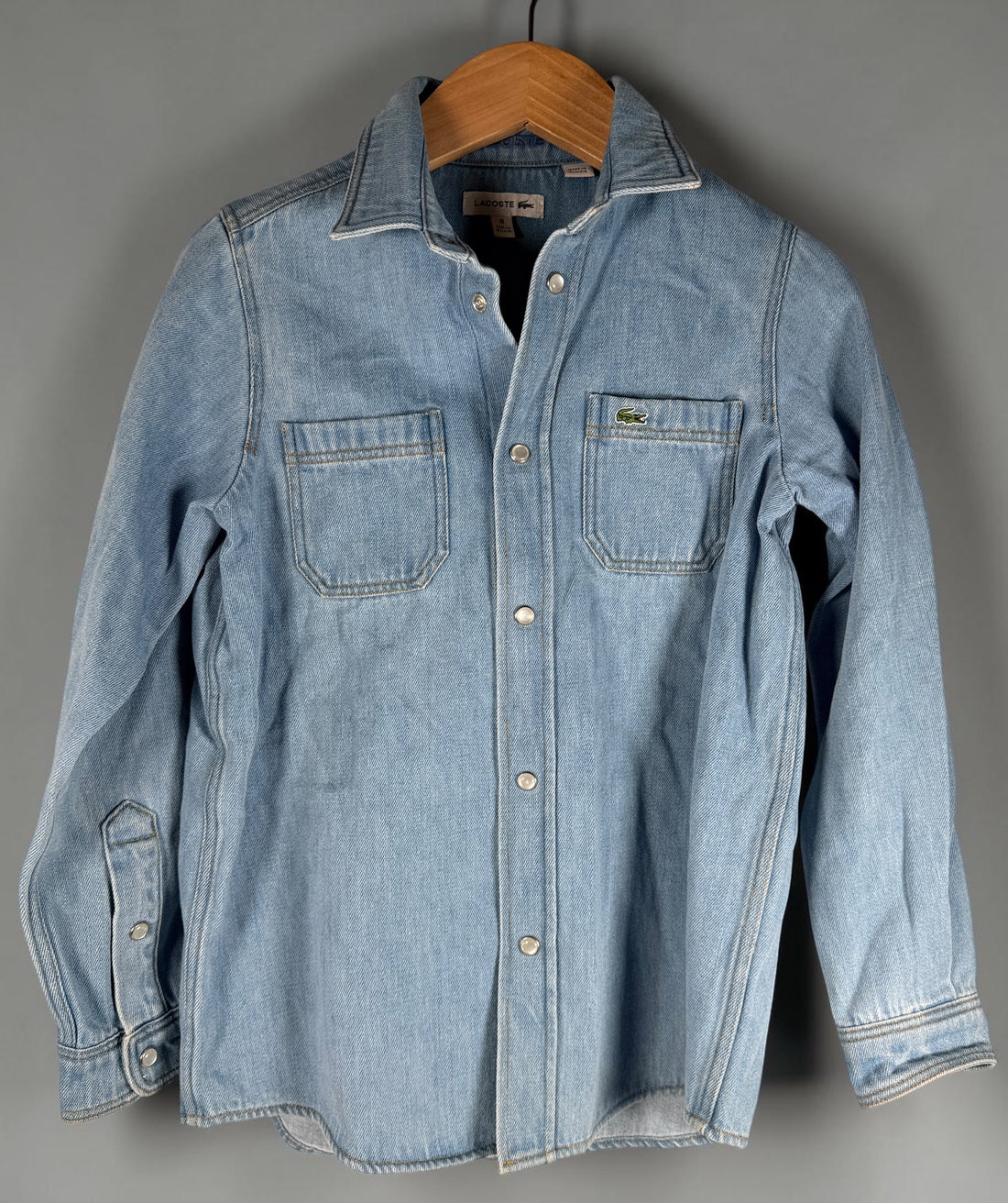 Authentic Lacoste kids denim overshirt in size 8 featuring snap-button closure, chest pockets, and classic crocodile logo. Light wash designer children’s wear.