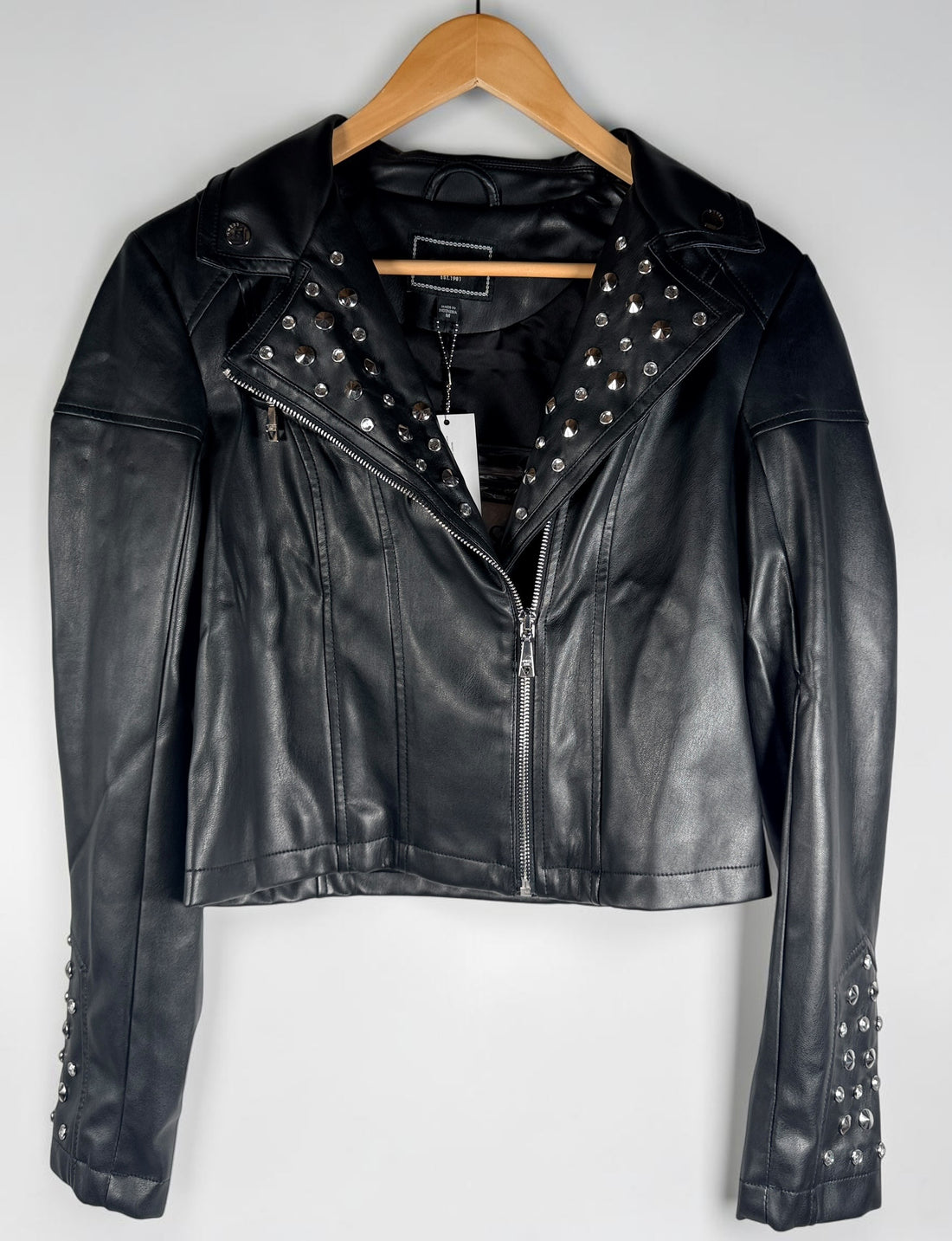 GUESS studded faux leather moto jacket in black, size medium. New with tags featuring rhinestone accents, asymmetrical zip closure and cropped biker styling.