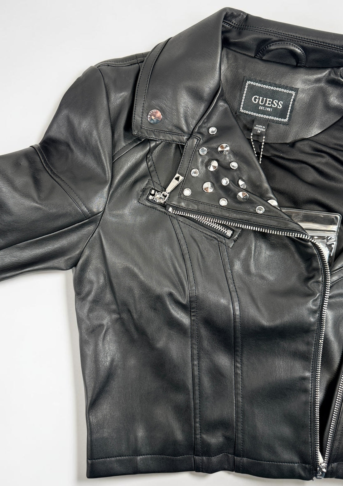 GUESS studded faux leather moto jacket in black, size medium. New with tags featuring rhinestone accents, asymmetrical zip closure and cropped biker styling.