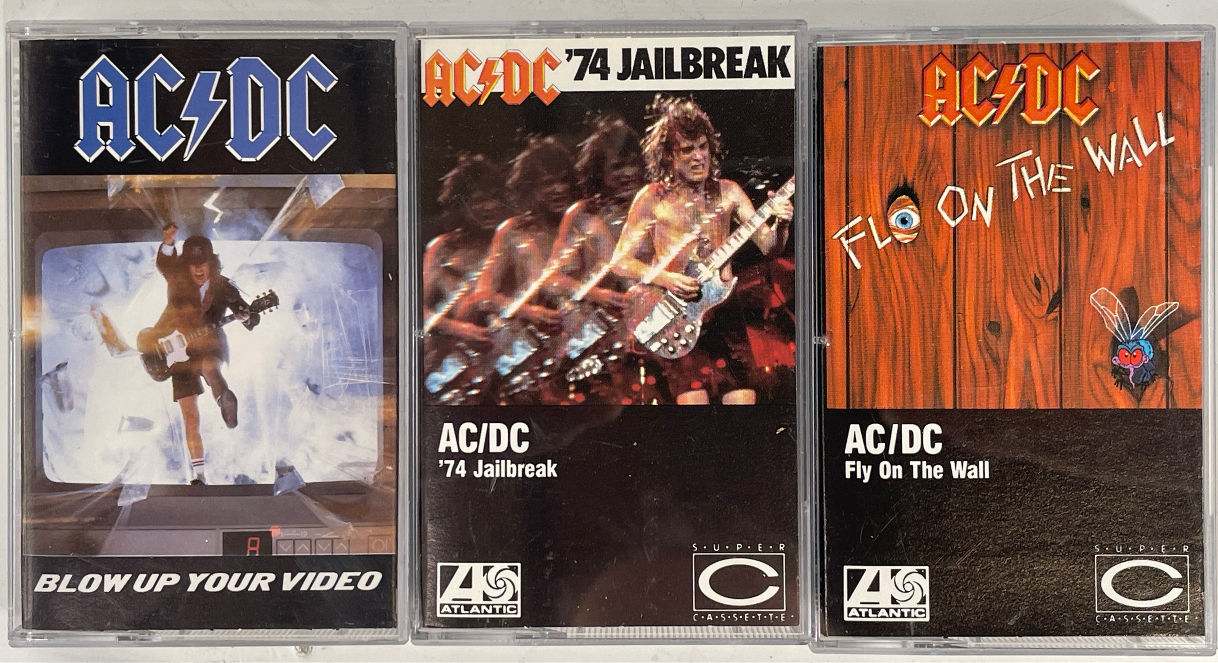 Three AC/DC cassette tapes with different covers on a white background