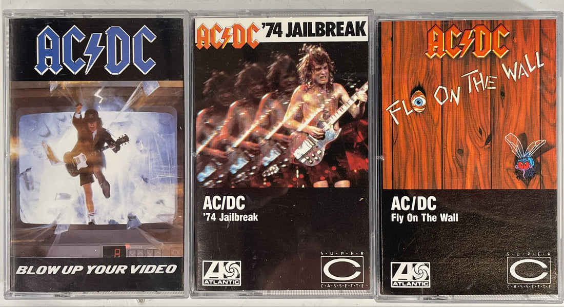 Three AC/DC cassette tapes with different covers on a white background