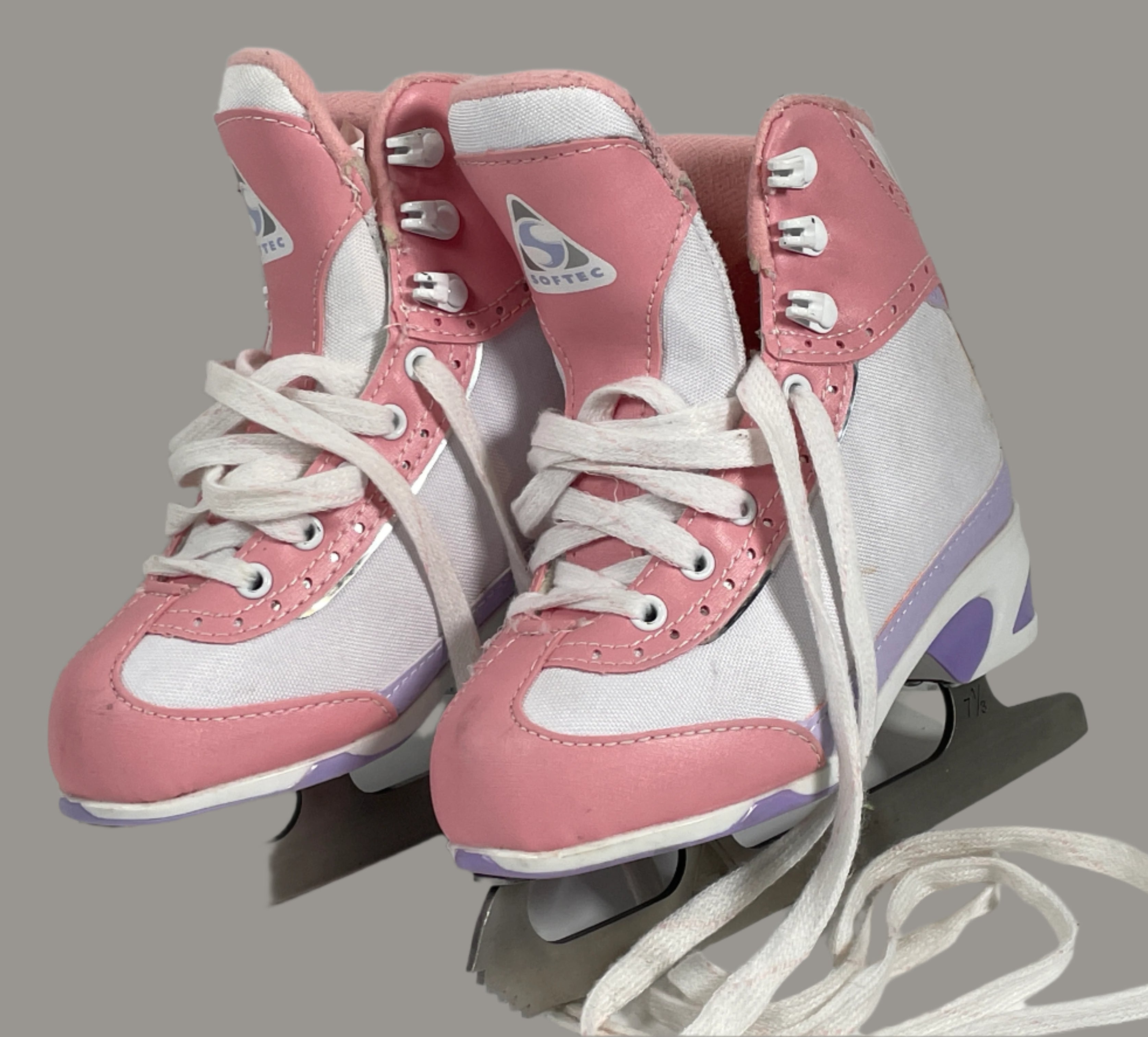 Pair of pink and white ice skates on a light gray surface with a white brick wall background.