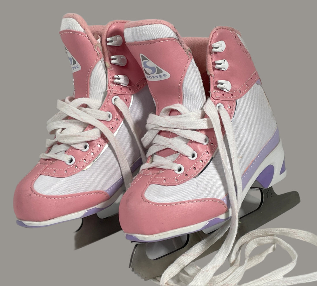 Pair of pink and white ice skates on a light gray surface with a white brick wall background.