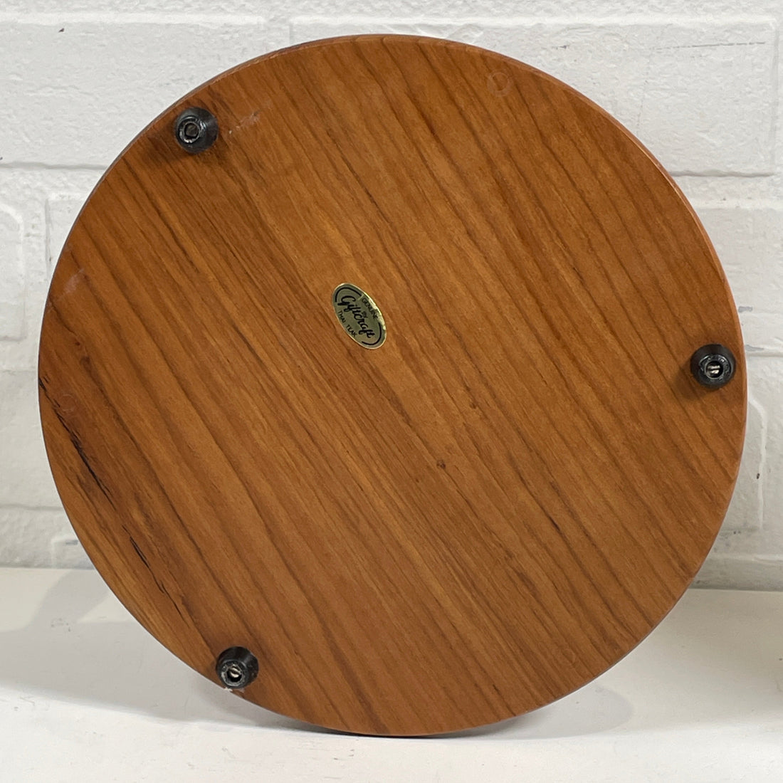 Wooden circular object with metal fixtures on a white brick wall background