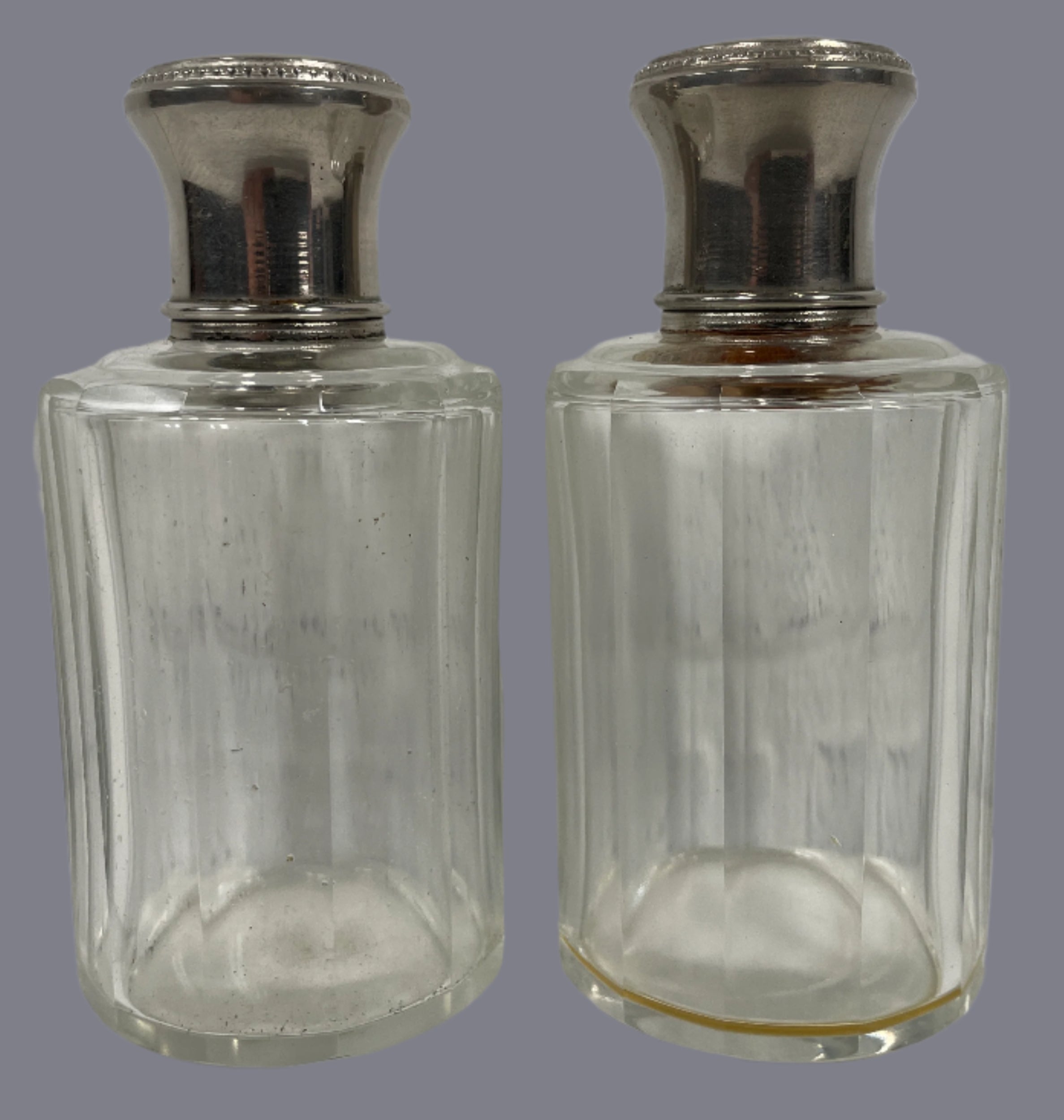 Two clear glass bottles with silver caps on a white surface and light gray background