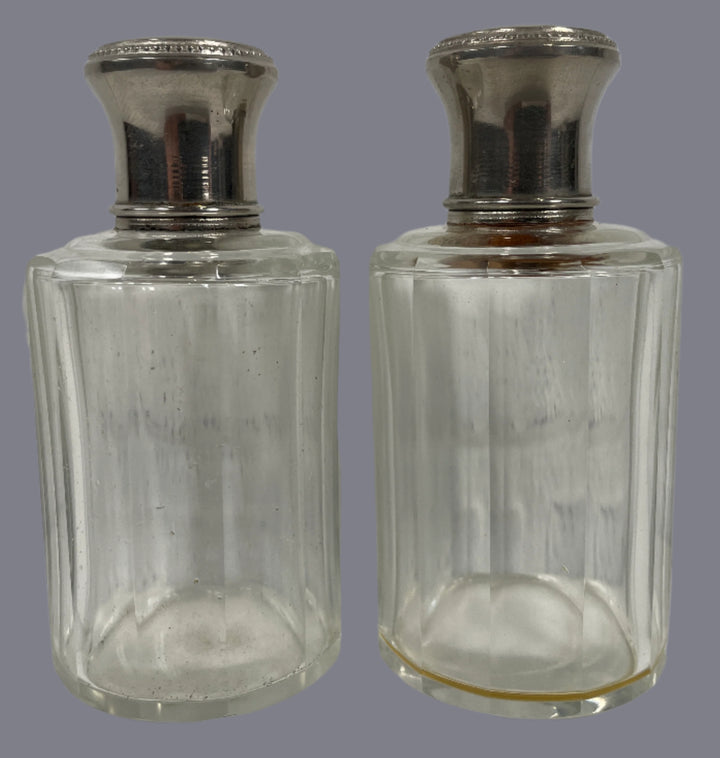 Two clear glass bottles with silver caps on a white surface and light gray background