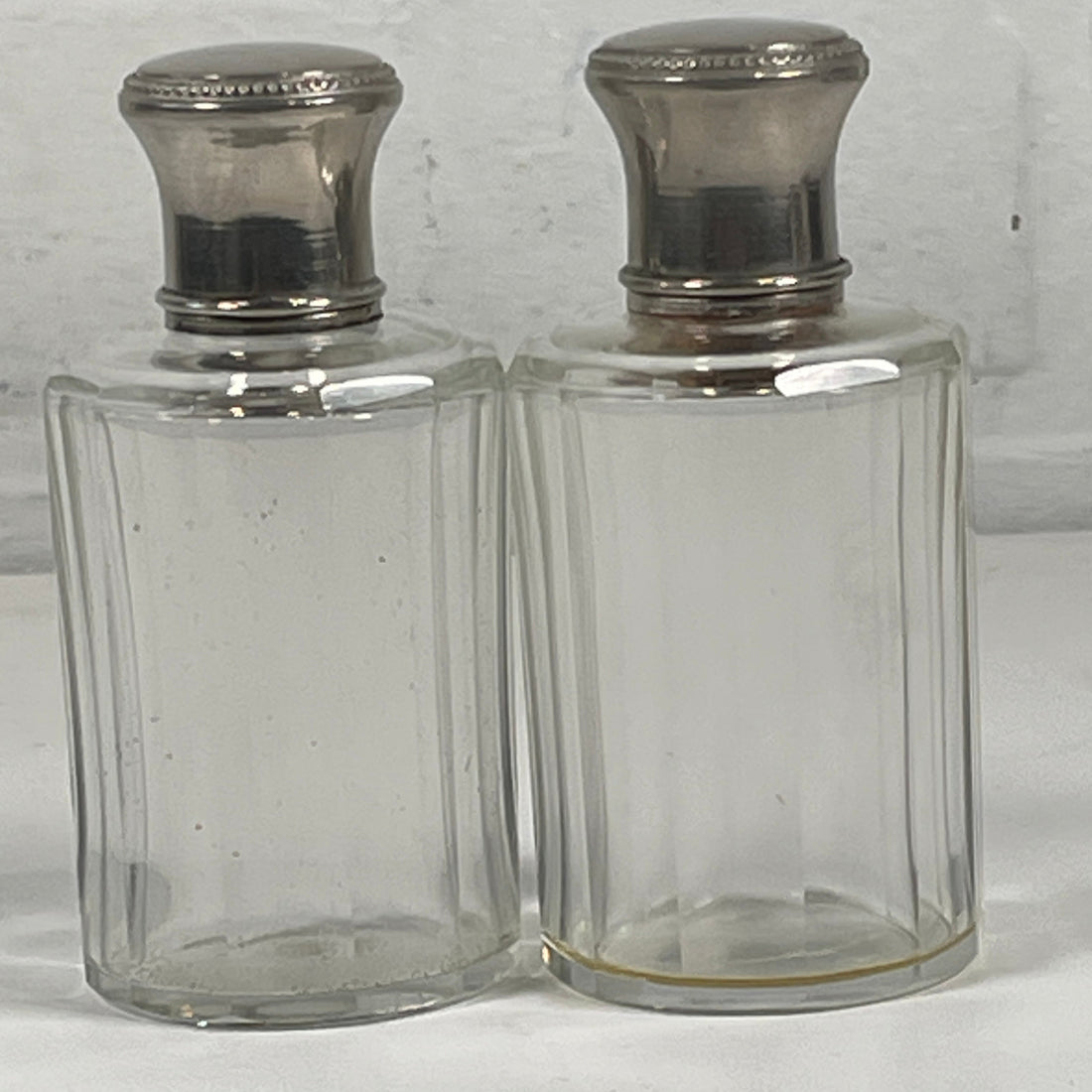 Clear glass decanter with silver stoppers on a white background