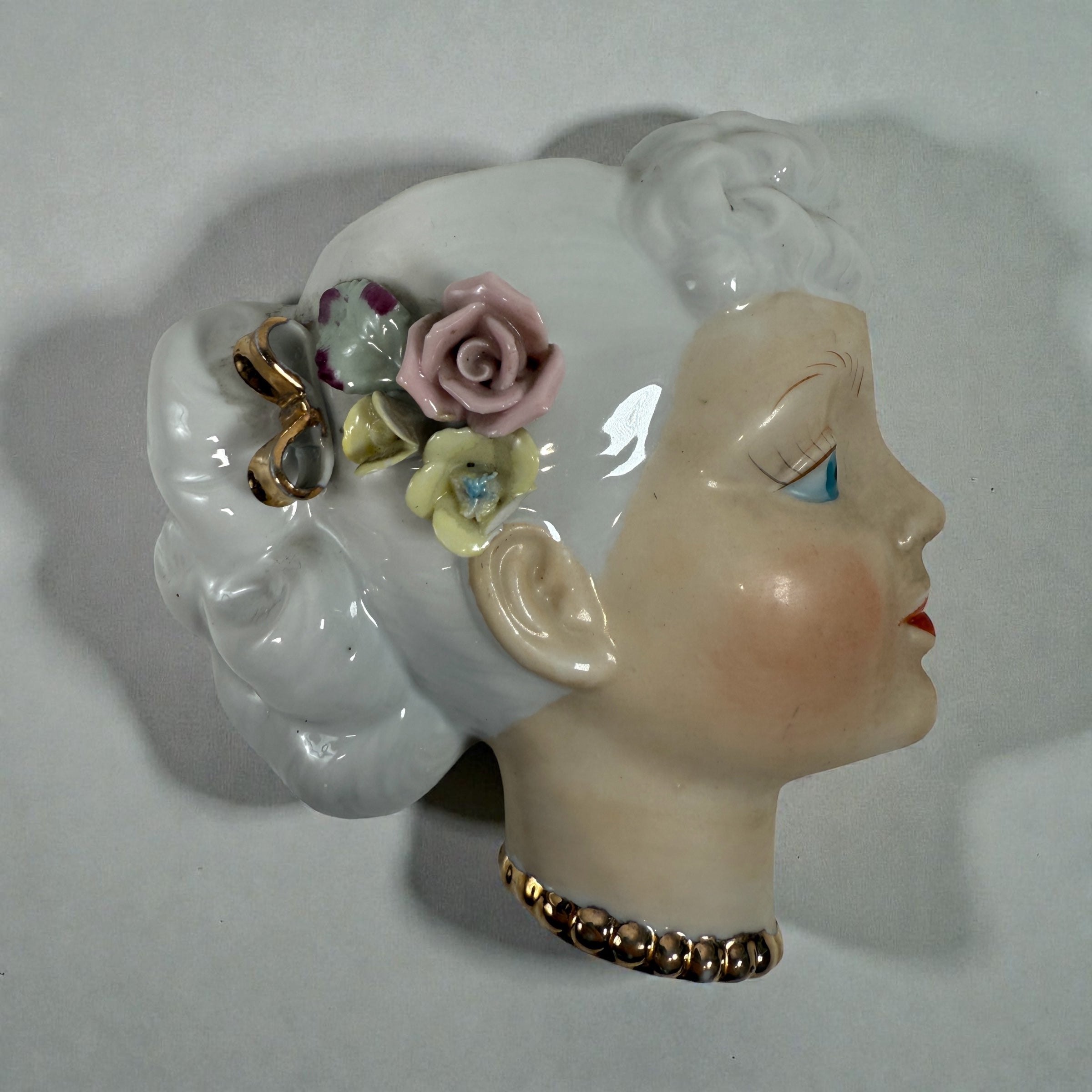 Mid-century Japanese porcelain lady-head wall mask with floral accents. Vintage décor piece with one chipped flower. Ideal for collectors and retro interiors.