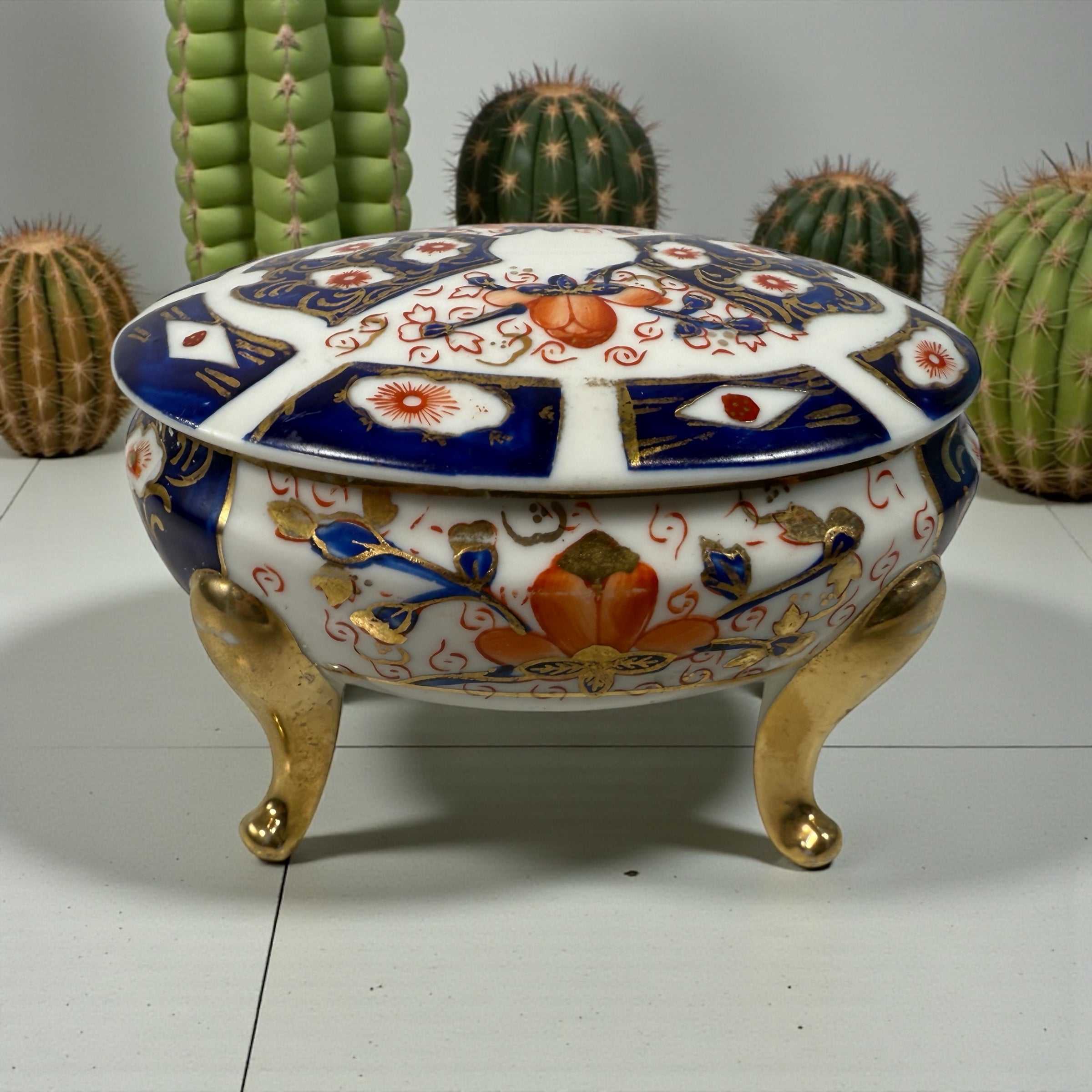 Japanese Imari style porcelain trinket box with lid and brass feet. Decorative vintage export ware in cobalt blue, red, and gilt accents.