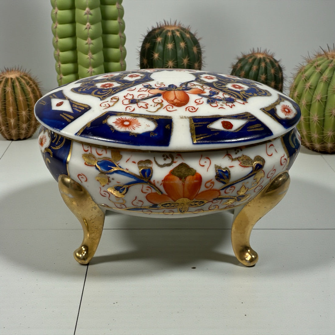 Japanese Imari style porcelain trinket box with lid and brass feet. Decorative vintage export ware in cobalt blue, red, and gilt accents.