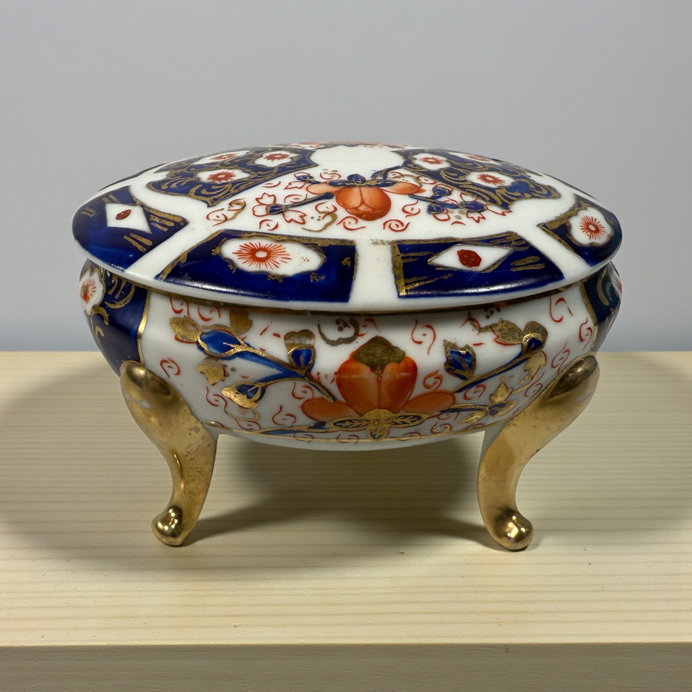Japanese Imari style porcelain trinket box with lid and brass feet. Decorative vintage export ware in cobalt blue, red, and gilt accents.