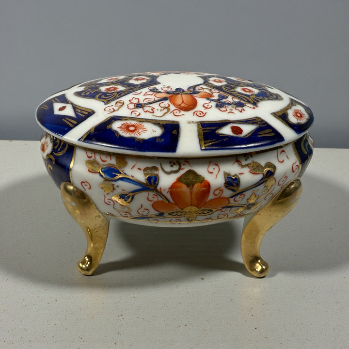 Japanese Imari style porcelain trinket box with lid and brass feet. Decorative vintage export ware in cobalt blue, red, and gilt accents.