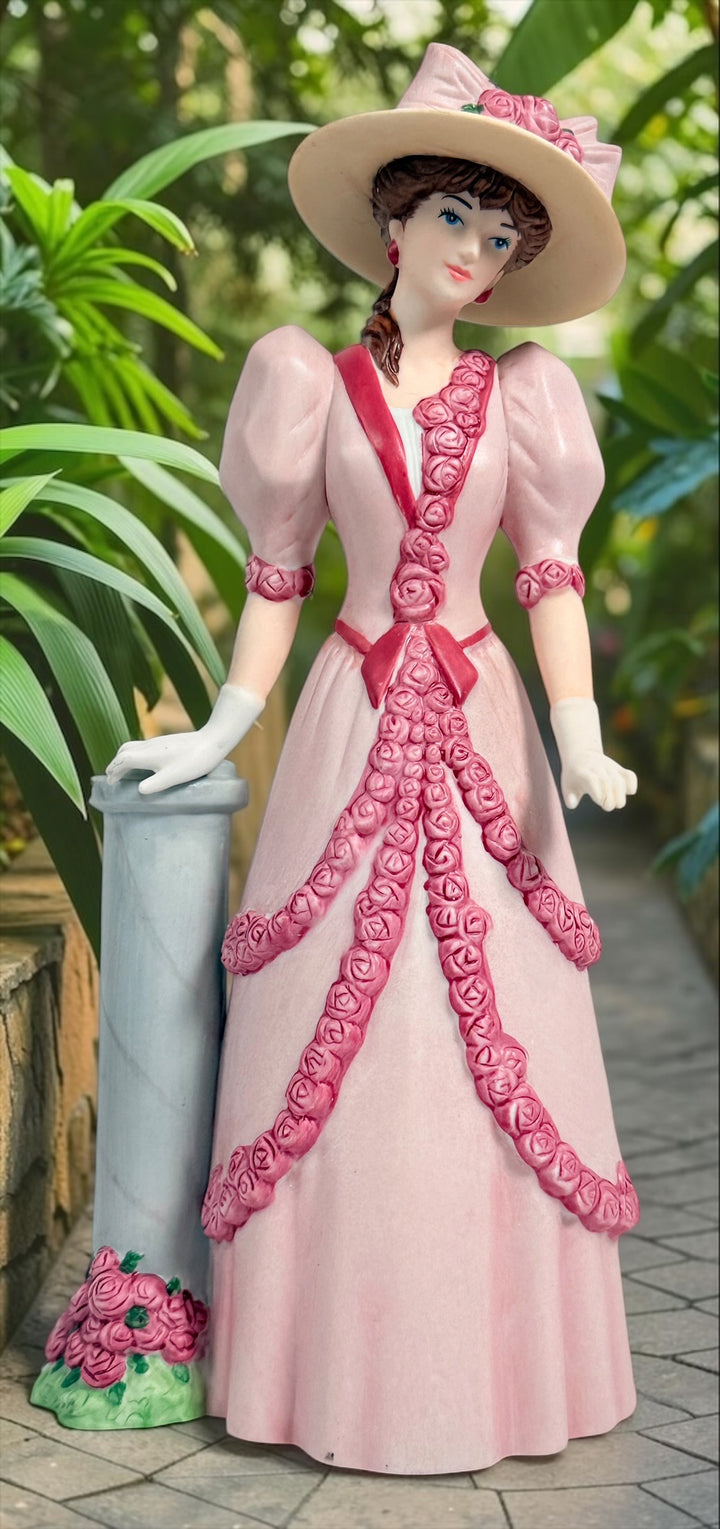 2015 Mrs. Albee Avon commemorative figurine featuring a Victorian lady in a pink rose-trimmed dress with marble-look column. Ceramic collectible award statue.