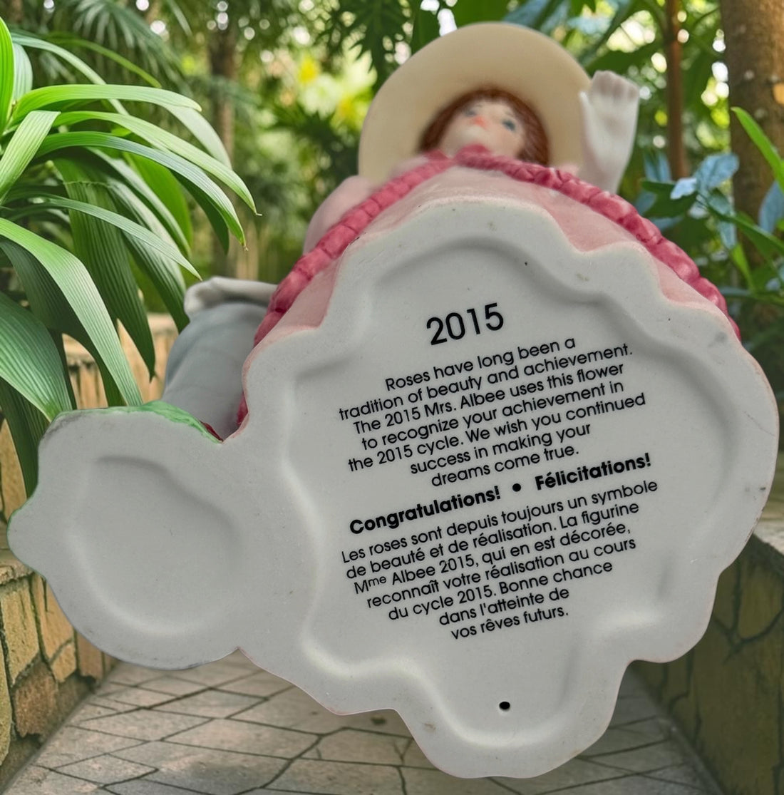 2015 Mrs. Albee Avon commemorative figurine featuring a Victorian lady in a pink rose-trimmed dress with marble-look column. Ceramic collectible award statue.