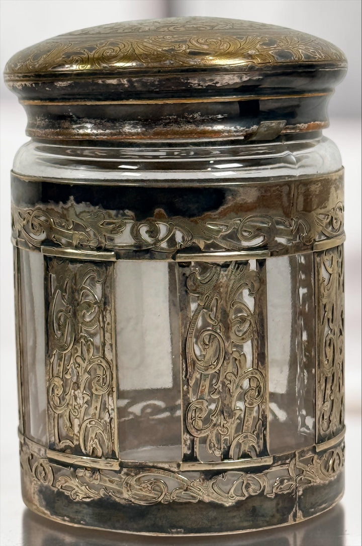 Antique Victorian glass tobacco humidor with ornate German silver overlay, engraved floral motifs, and domed lid. Elegant late-19th-century decorative storage jar.