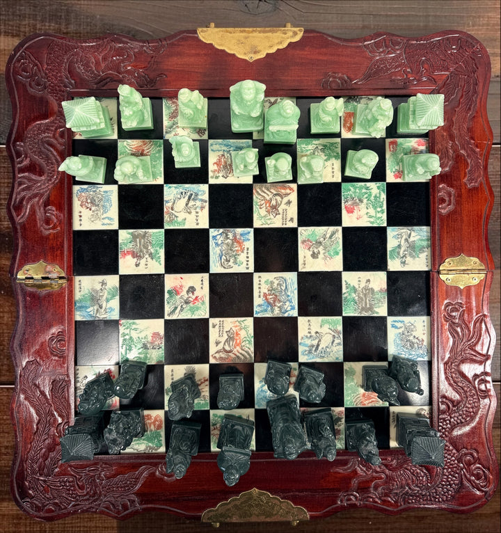 Vintage Chinese 32-piece figural chess set with jade-coloured pieces, carved dragon folding wood board, illustrated squares and fitted storage.