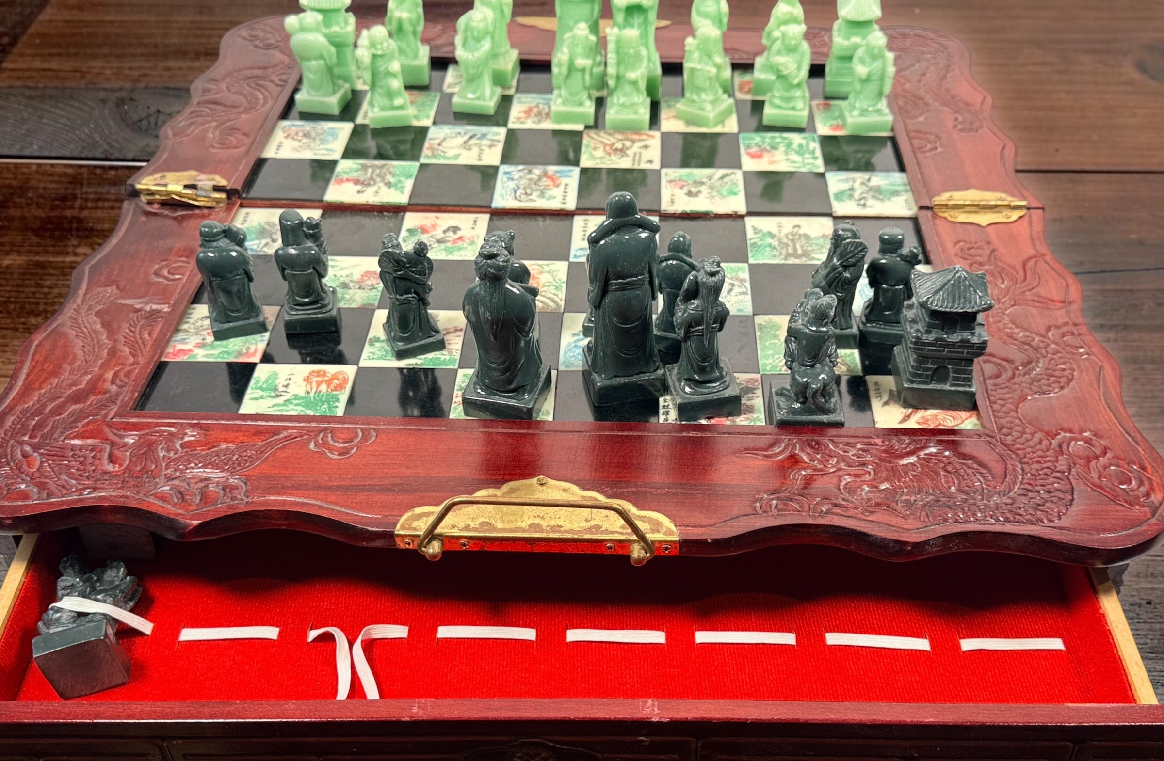 Vintage Chinese 32-piece figural chess set with jade-coloured pieces, carved dragon folding wood board, illustrated squares and fitted storage.