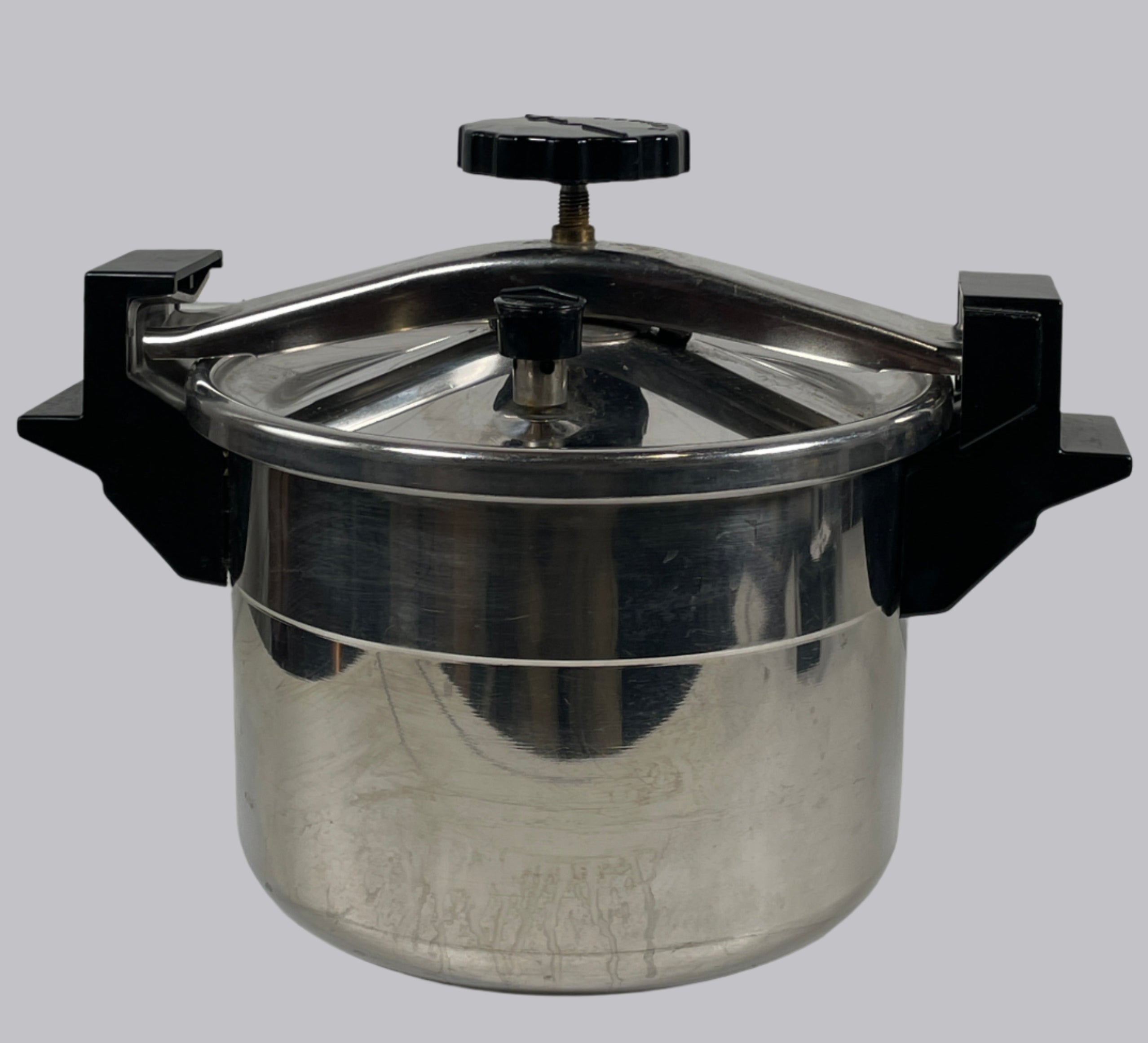Metal pressure cooker on a white tiled wall
