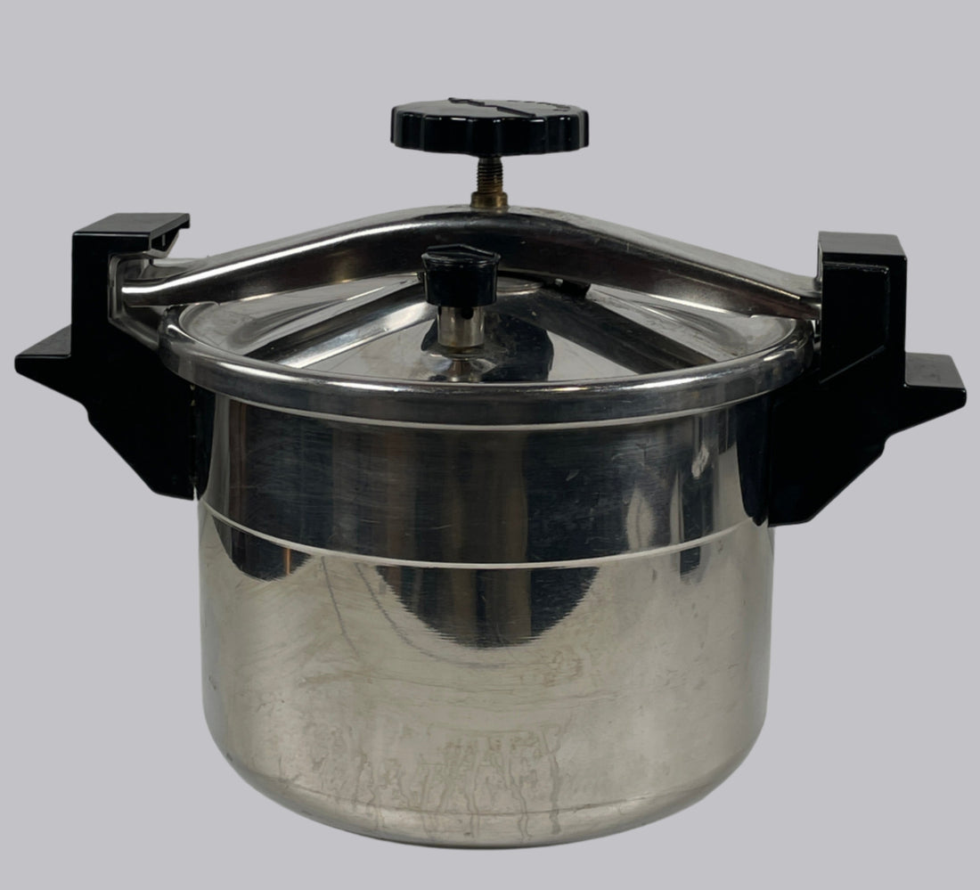 Metal pressure cooker on a white tiled wall