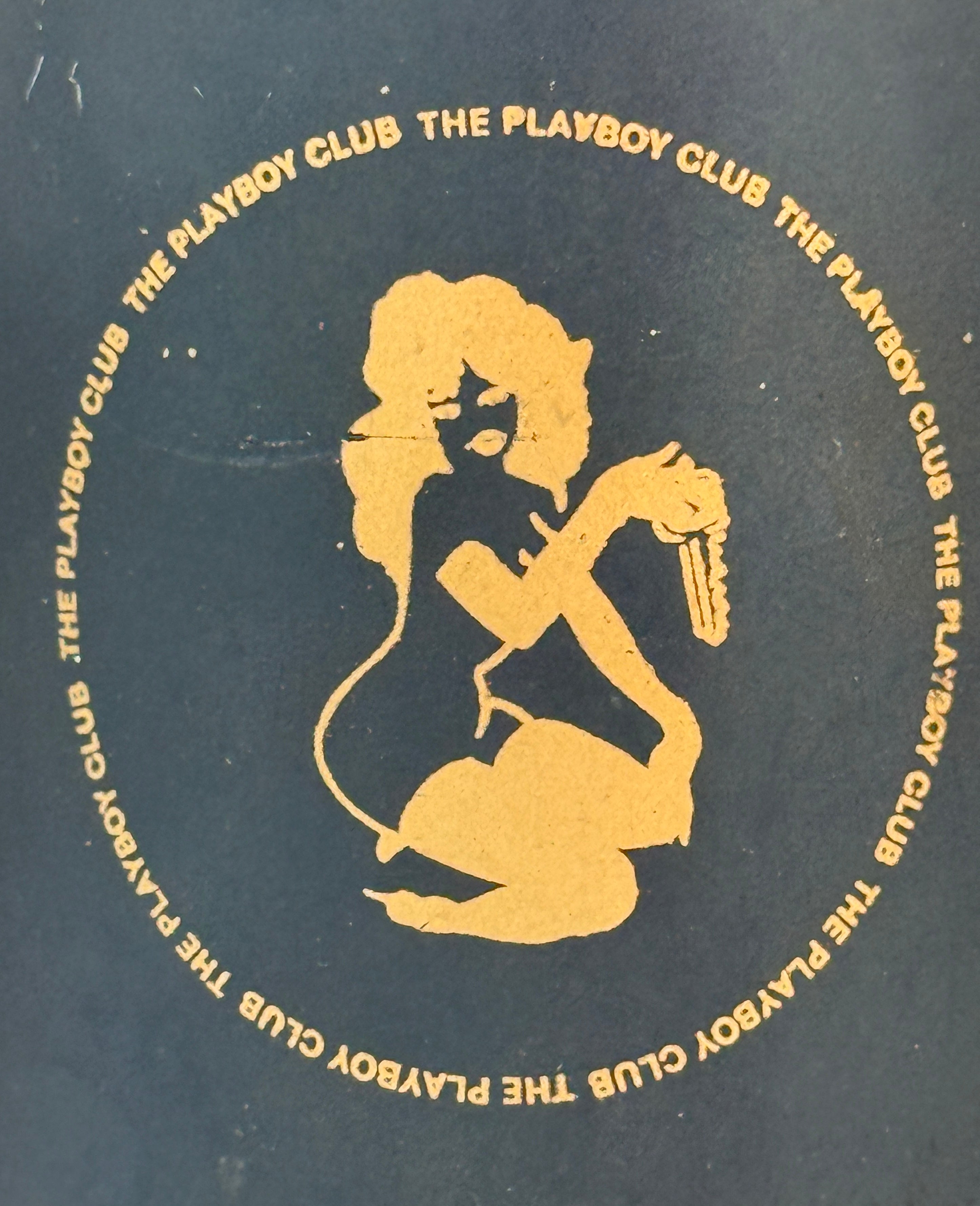 Gold silhouette of a woman with a gun on a black background with 'The Playboy Club' text.