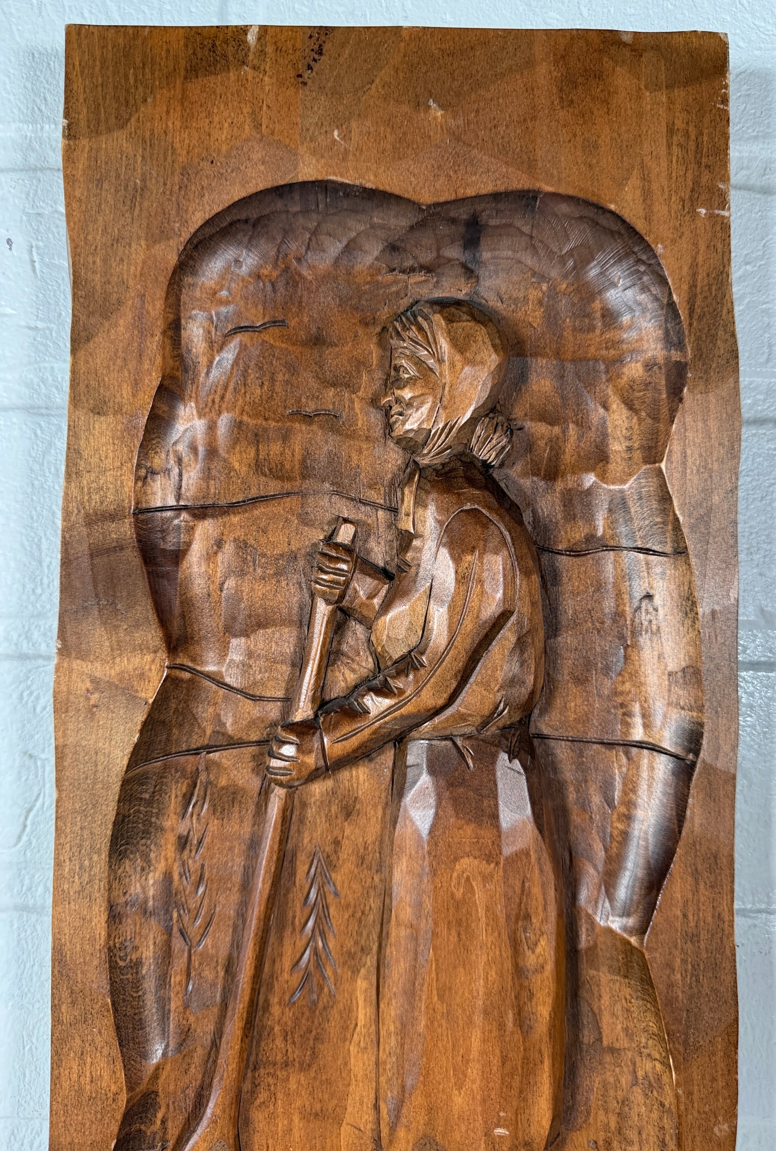 Wooden relief sculpture of a person holding a staff on a wooden panel.