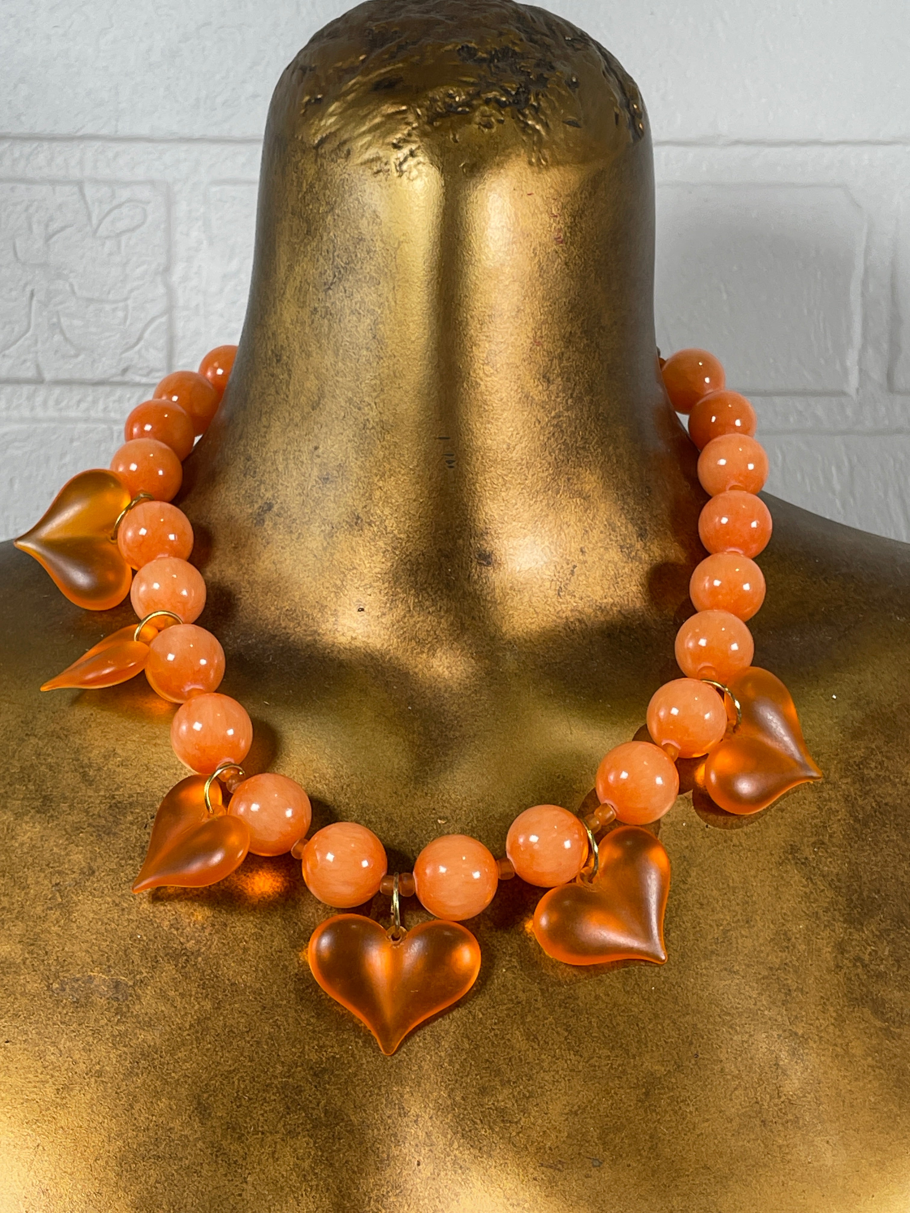 Orange beaded bracelet on a gold mannequin bust against a neutral background