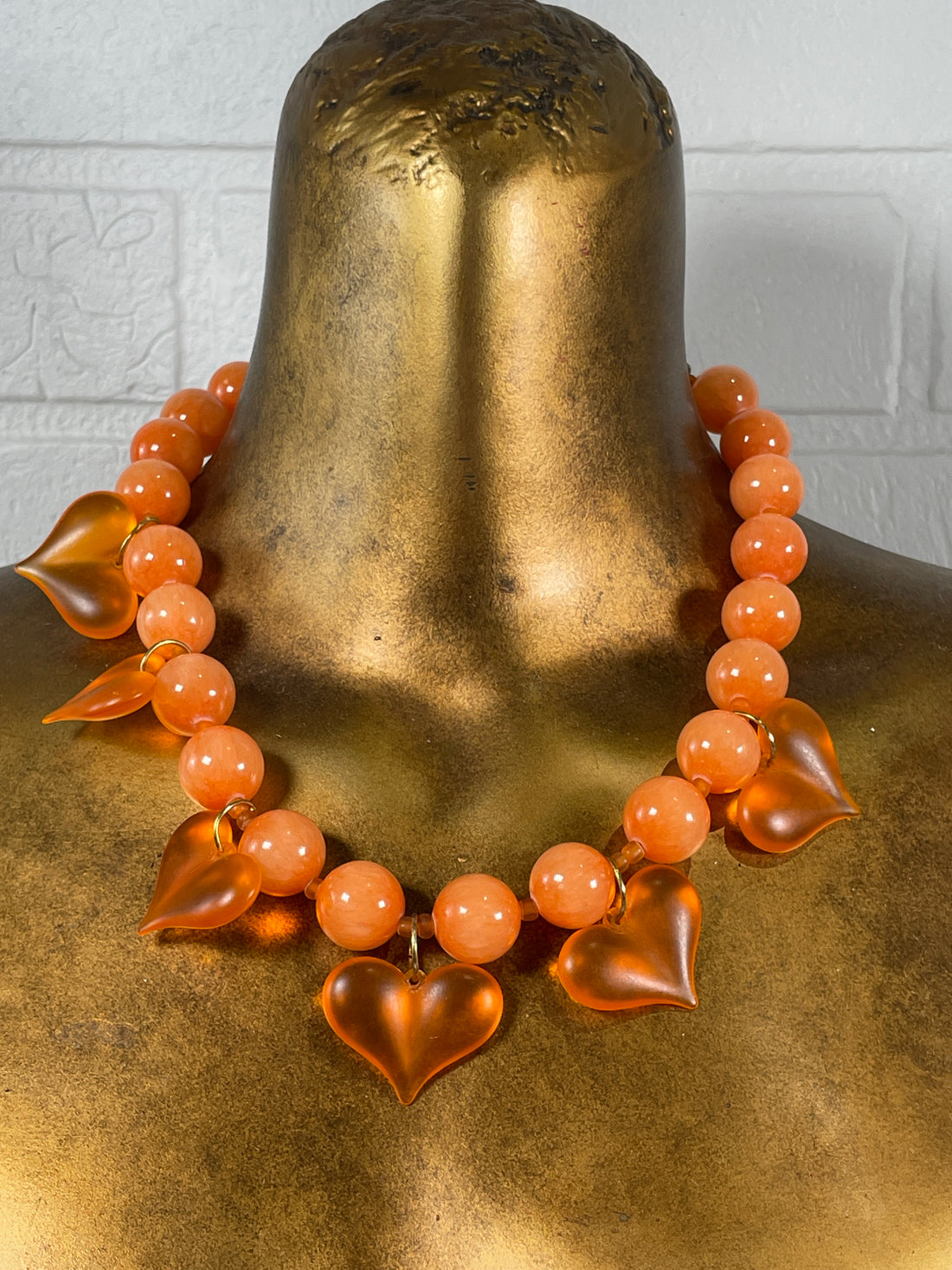 Orange beaded bracelet on a gold mannequin bust against a neutral background