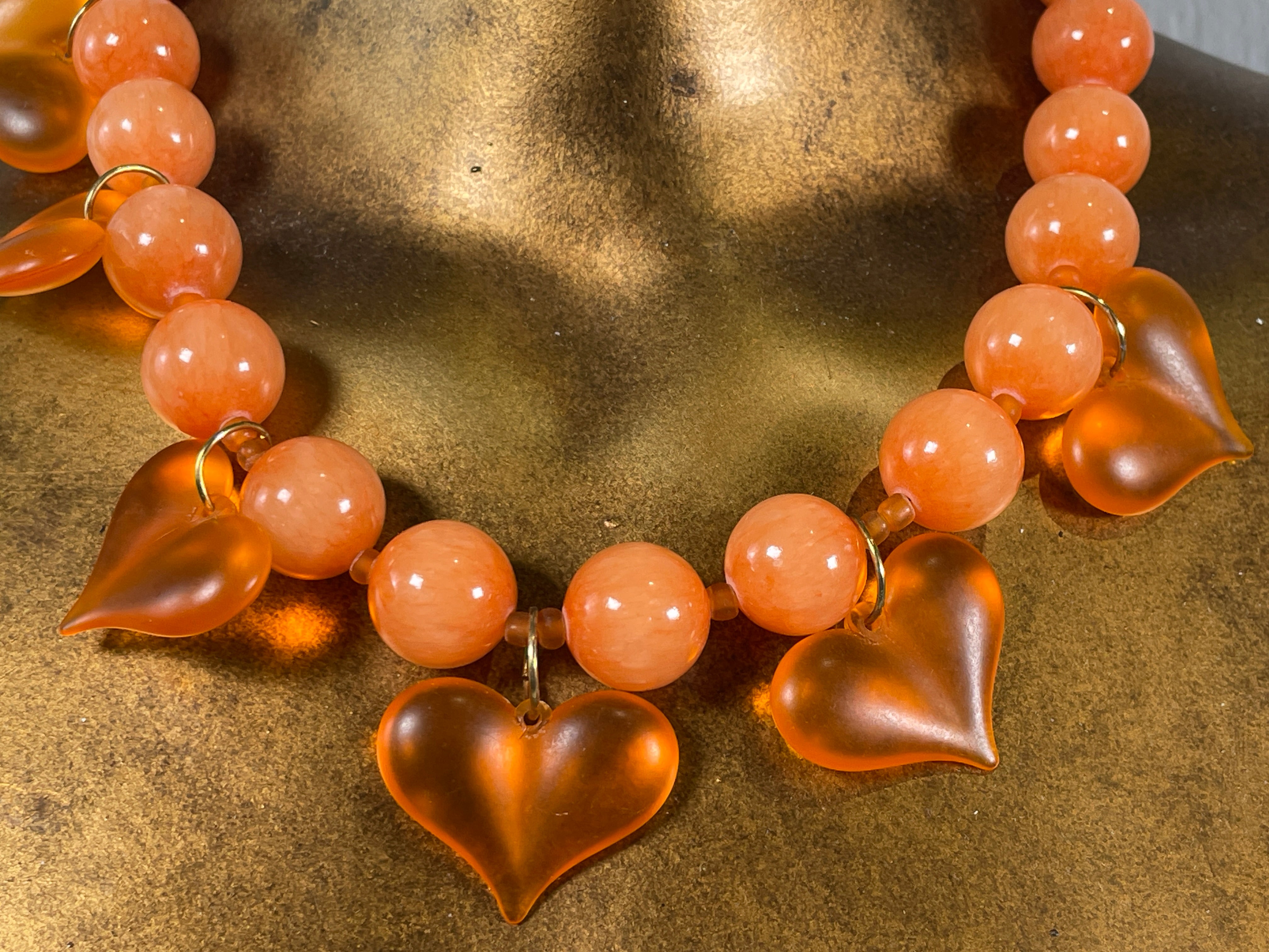 Necklace with heart-shaped and round peach-colored beads on a textured surface