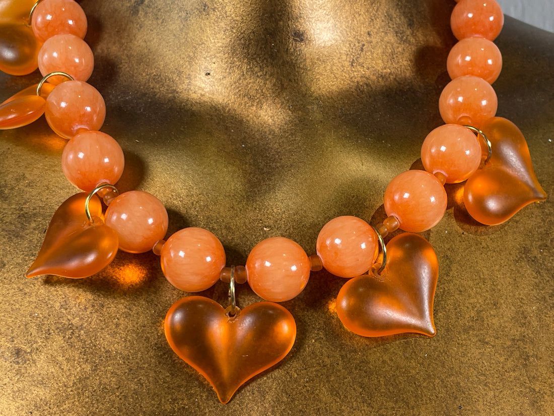 Necklace with heart-shaped and round peach-colored beads on a textured surface