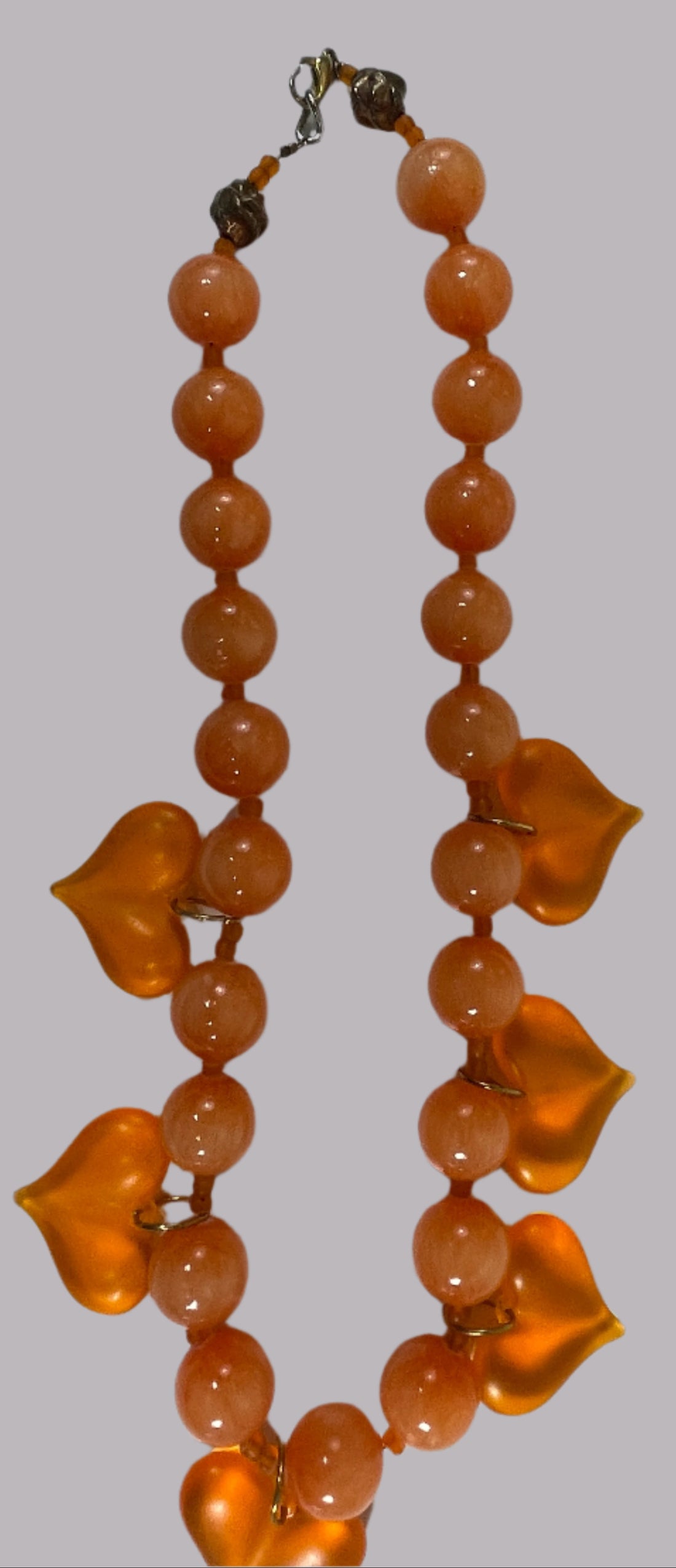 Orange beaded necklace with heart-shaped charms on a white background