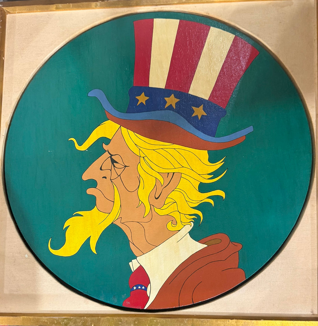 Circular portrait of long-haired Uncle Sam against a green background in a square gold-tone frame.